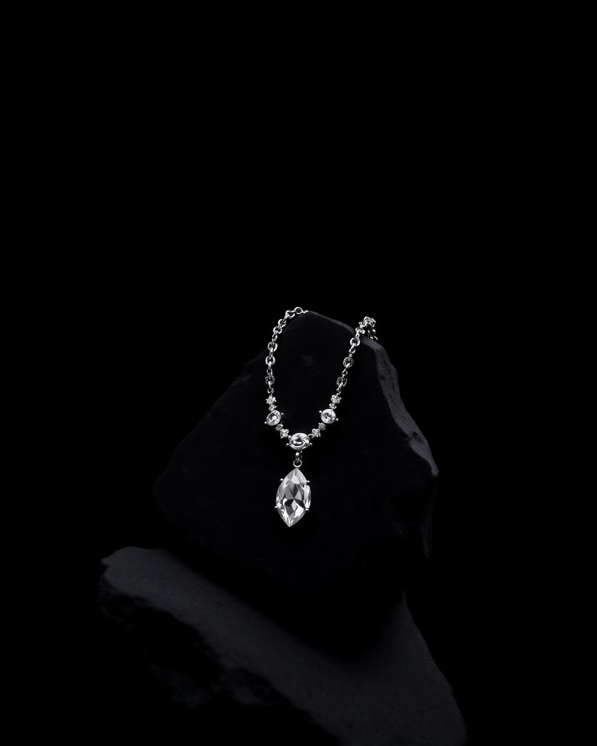 Diamond pendant necklace draped over dark stone